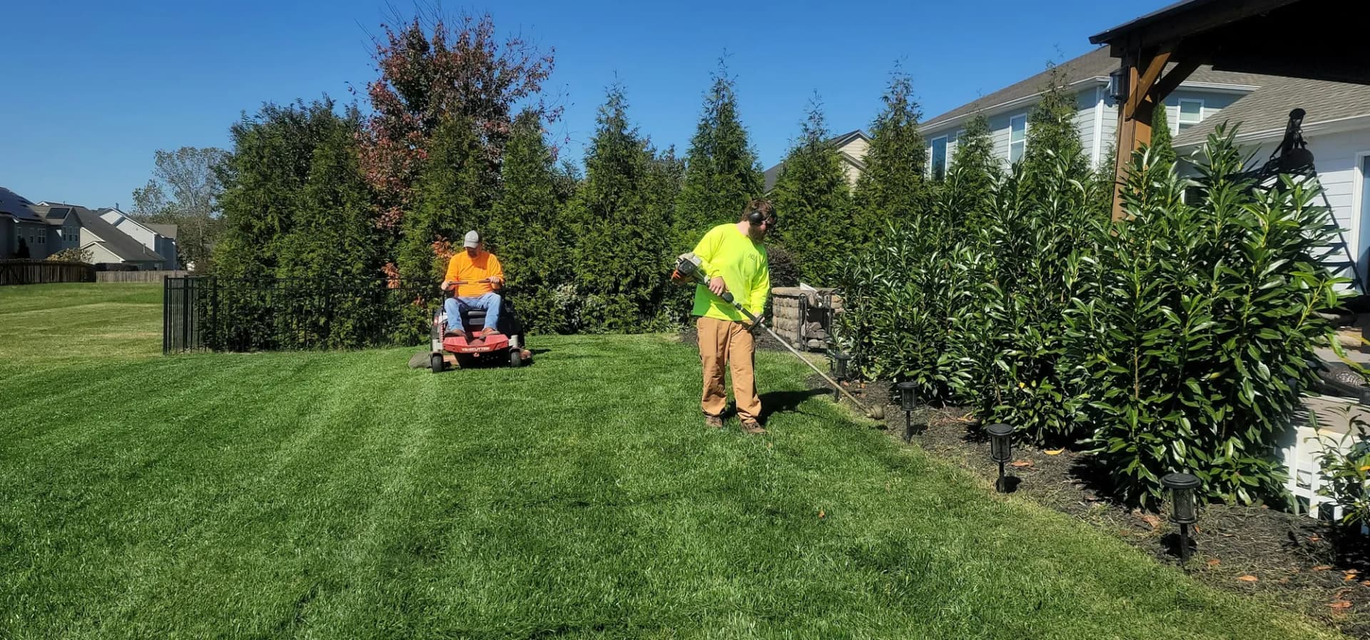 Two-person crew mowing and trimming a striped front lawn
