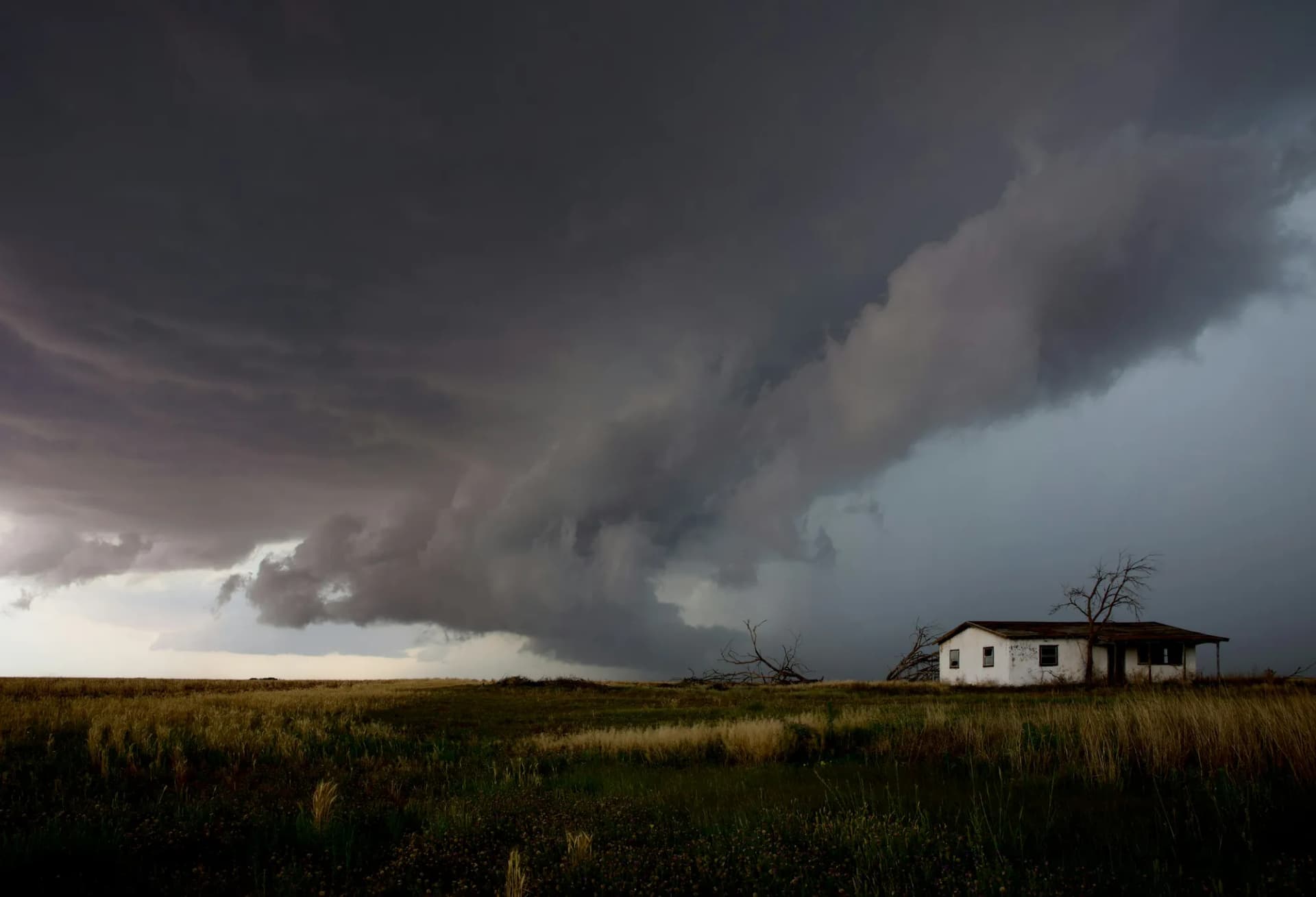 Dark storm cloud building over a single house on open land