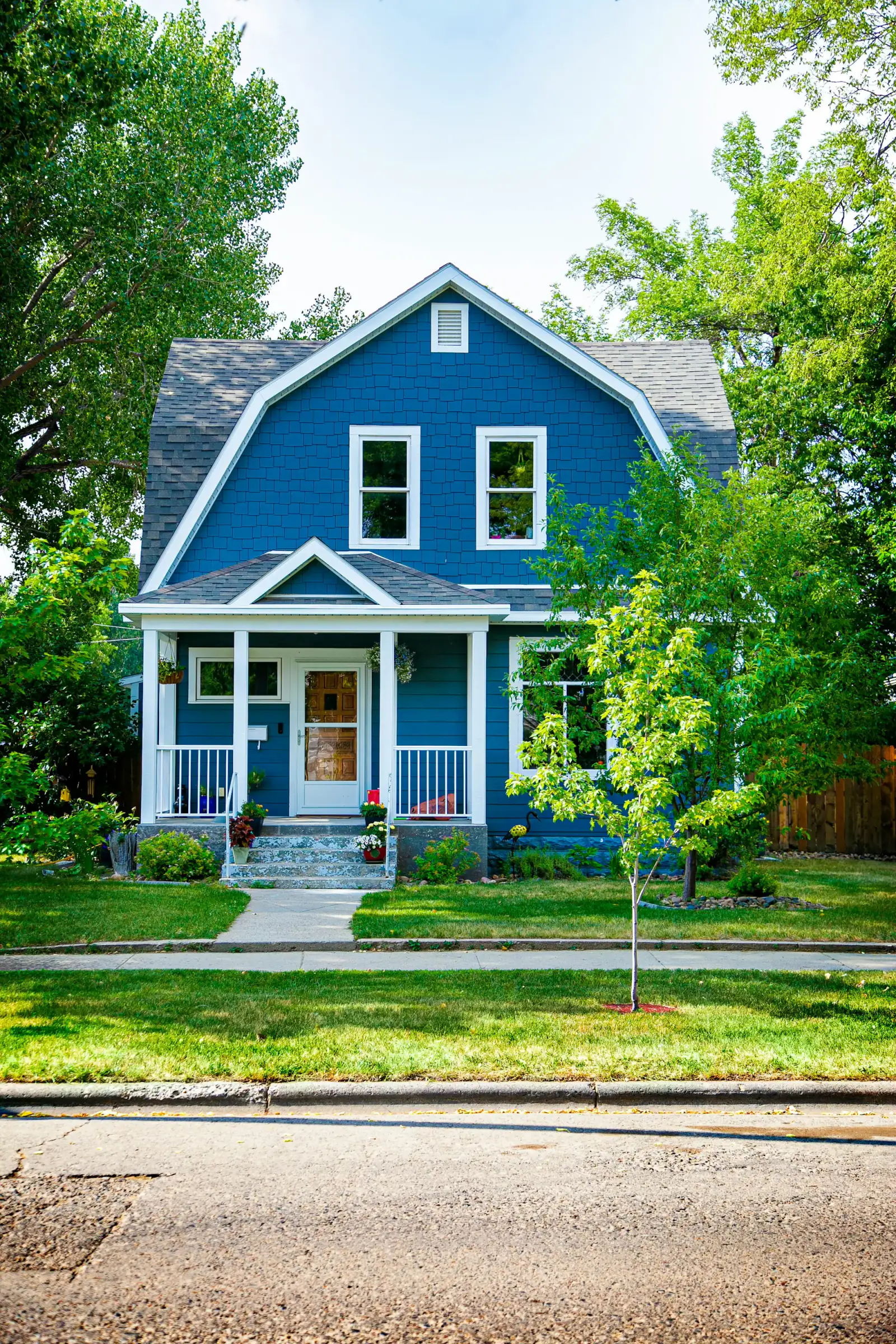 Blue two-story house with a trimmed front lawn and young tree