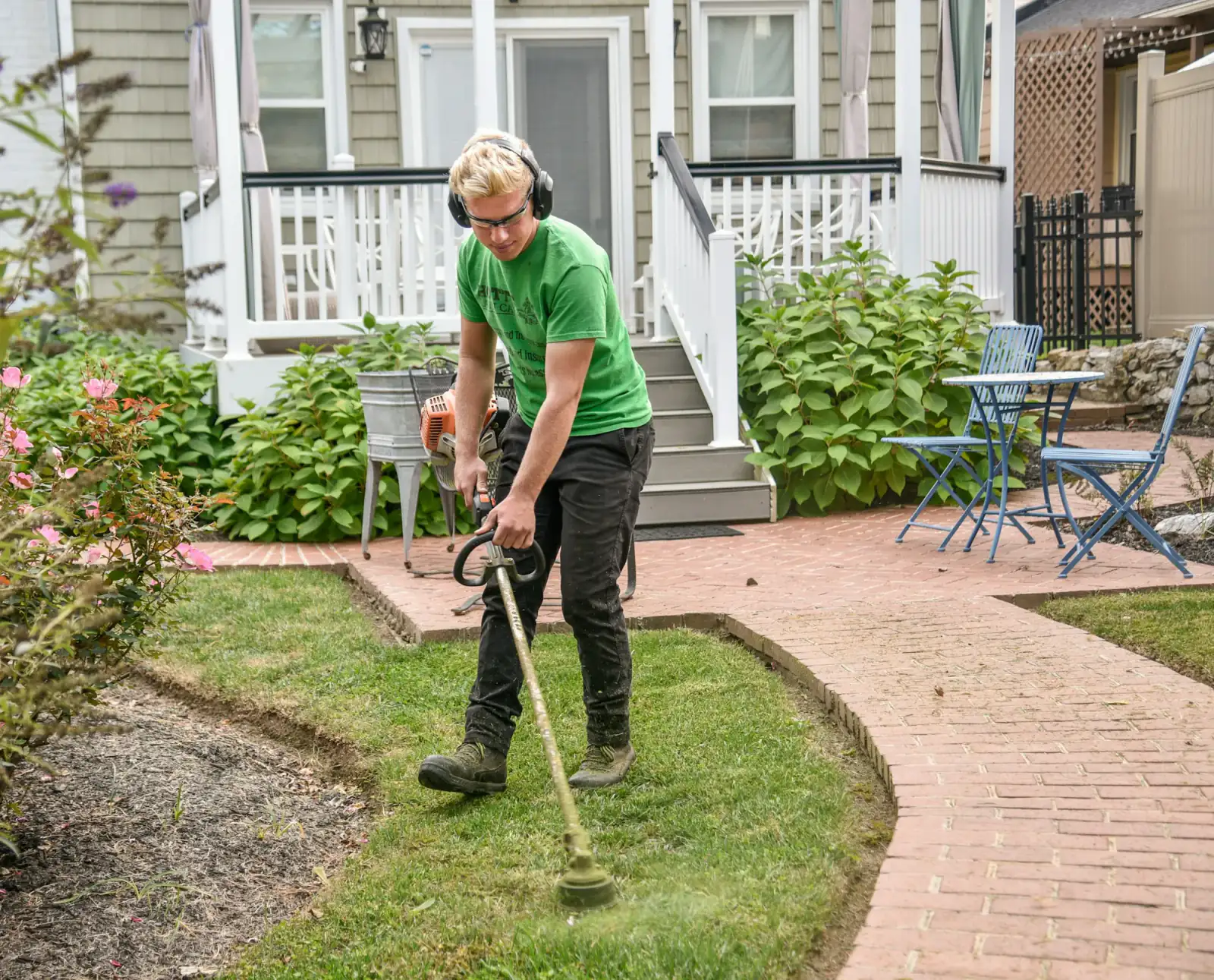 Crew member edging a lawn beside a brick walkway