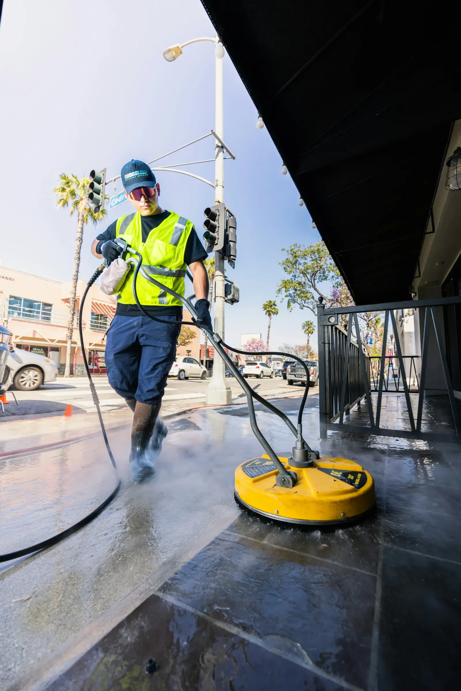 Technician running a rotary surface cleaner across wet pavement