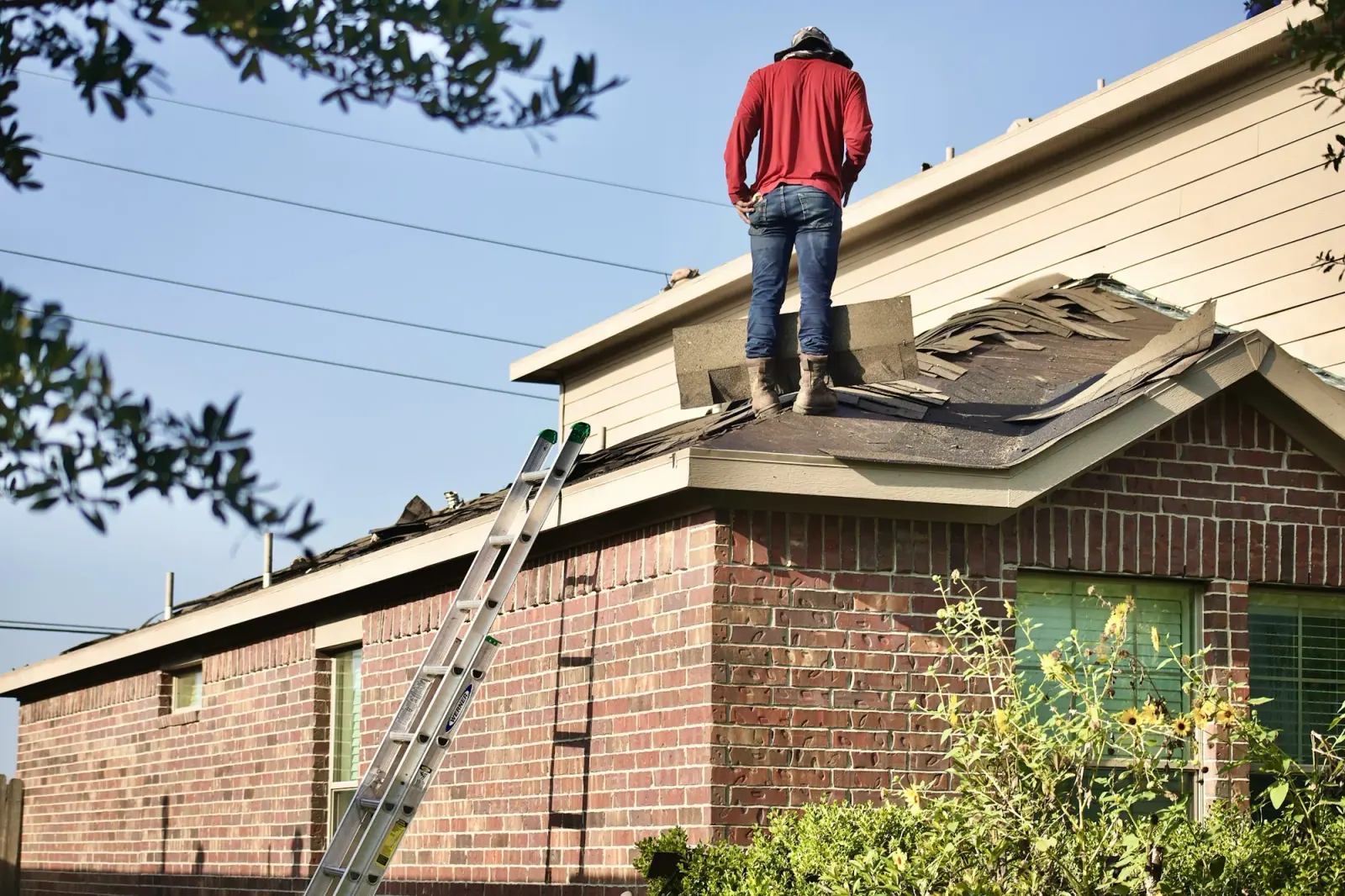 Roofer standing on a storm-damaged roof above a brick house