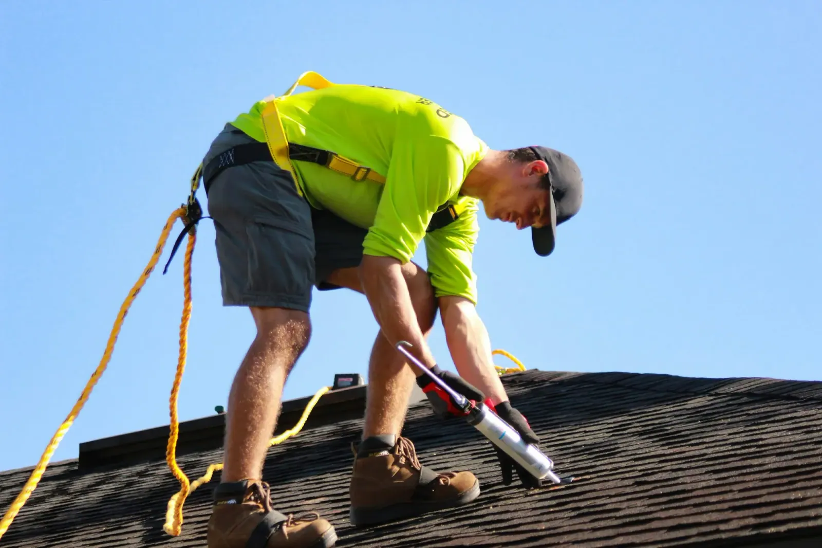 Roofer in a harness sealing shingles near the roof edge