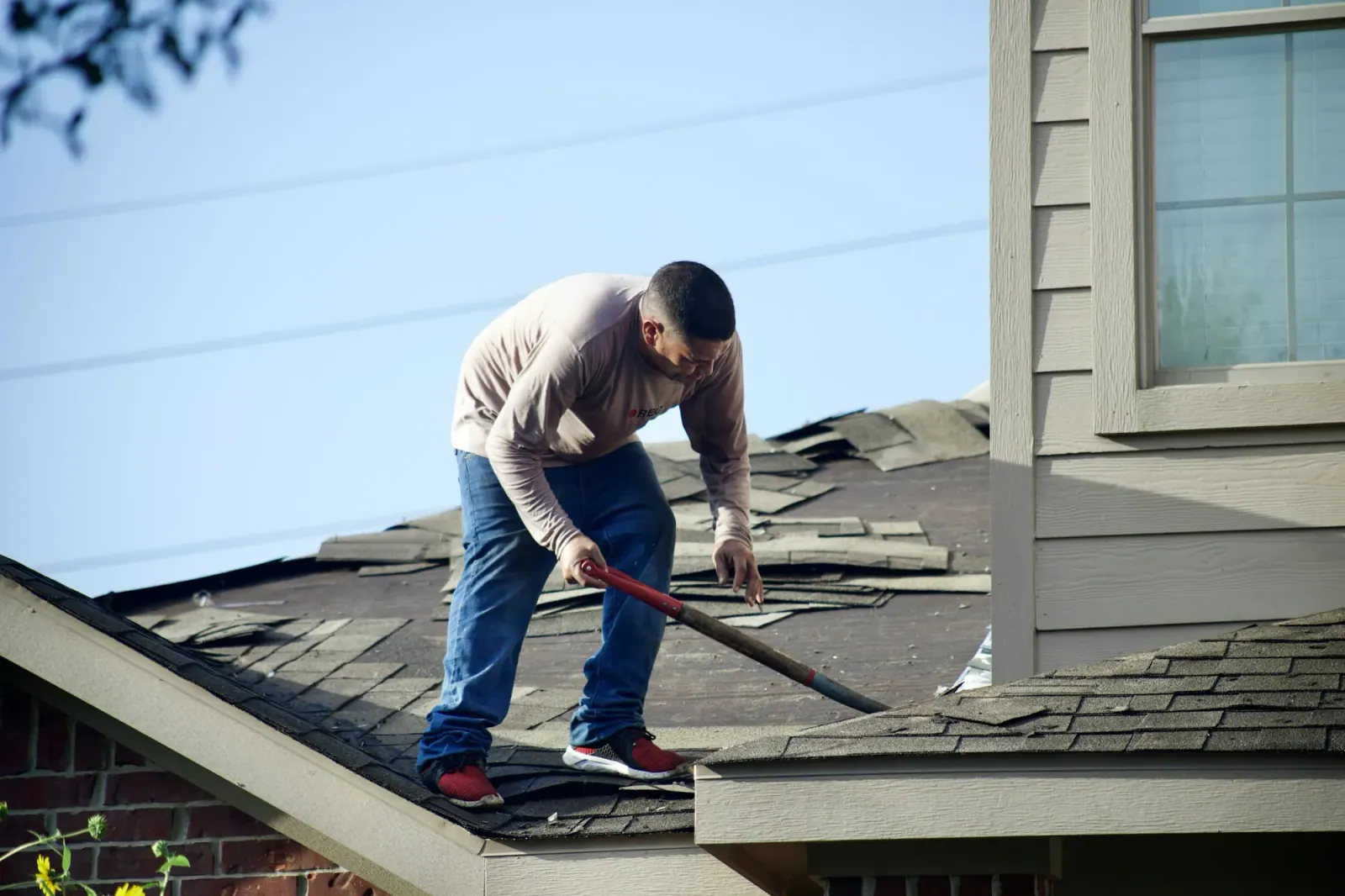 Worker tearing off old shingles from a residential roof