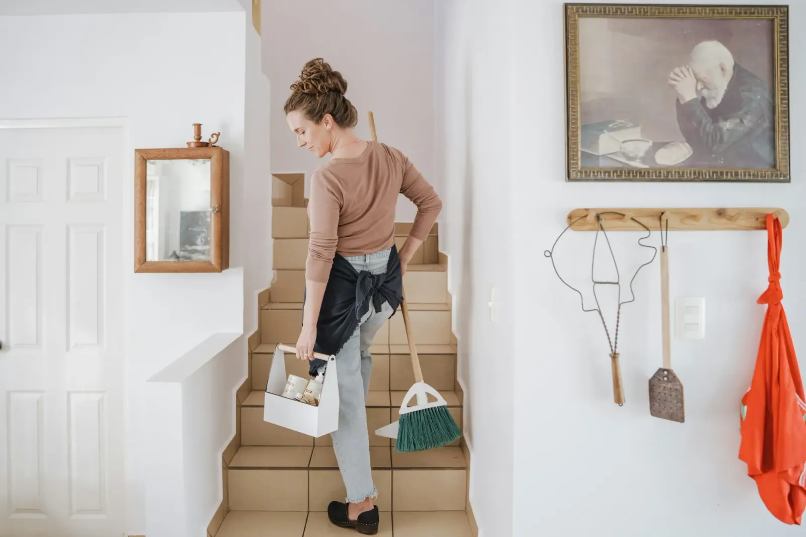 Cleaner carrying a caddy and broom up a staircase